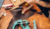 Leather Craft Or Leather Working. Selected Pieces Of Beautifully Colored Or Tanned Leather On Leather Craftman'S Work Desk . Piece Of Hide And Working Tools On A Work Table.